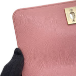 A close-up of a pink caviar leather CHANEL Coco handle with a gold-tone metal clasp engraved with the Chanel logo