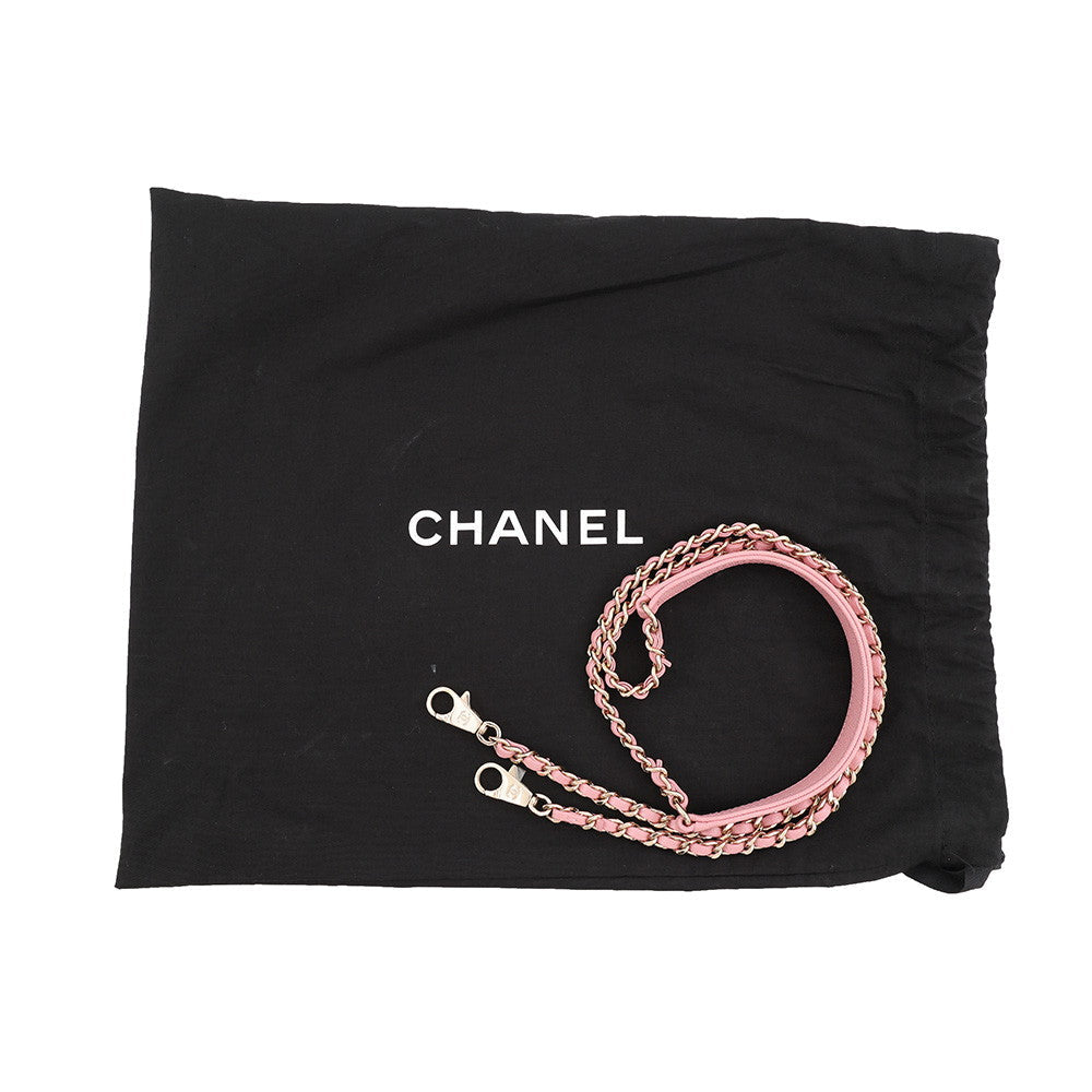 A pink leather and chain shoulder strap with gold-toned hardware, displayed on a black Chanel dust bag with the white CHANEL logo.