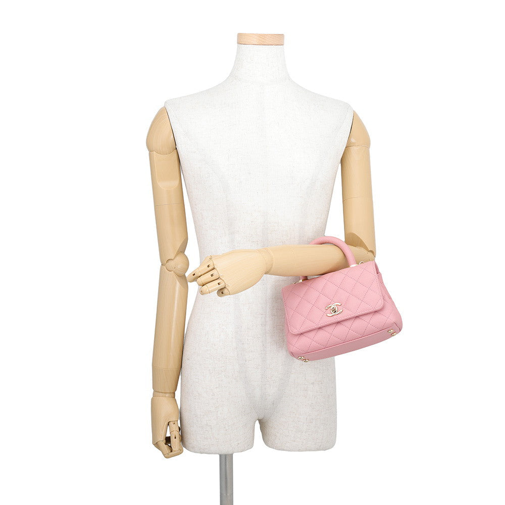 CHANEL Coco Handle Mini in Pink Caviar Leather with Gold-Tone Hardware displayed on a beige mannequin torso against a white background.