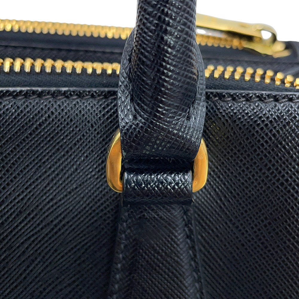 Close-up of Prada Gallerie black textured leather handbag with a gold-tone zipper and gold hardware, showing the handle attachment and material detail.