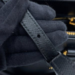 Close-up of Prada Saffiano Leather Galleria  black textured leather strap being held by black knit gloves, with a small gold-tone metal rivet visible on the strap.