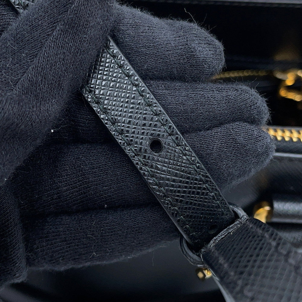 Close-up of Prada Saffiano Leather Galleria  black textured leather strap being held by black knit gloves, with a small gold-tone metal rivet visible on the strap.