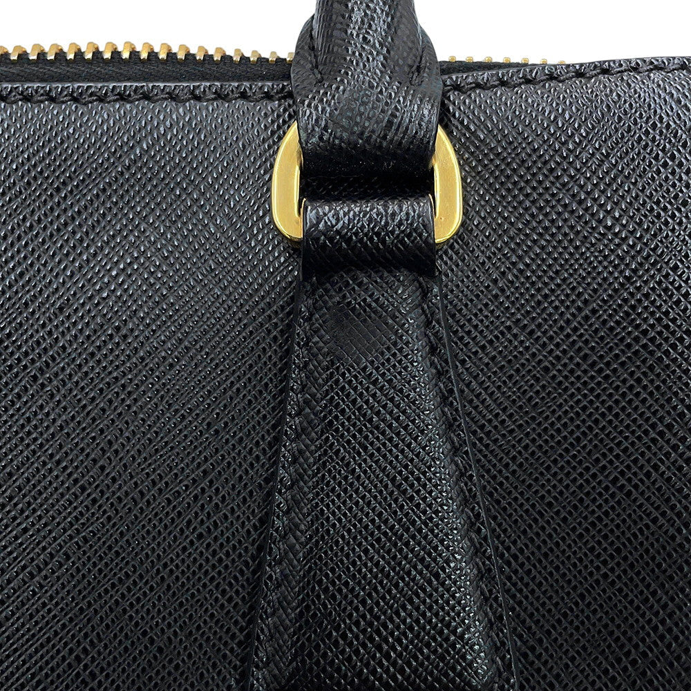 Close-up of a Prada Saffiano Leather Galleria black textured leather handbag featuring a top handle with a gold-tone metal loop and zipper pull.
