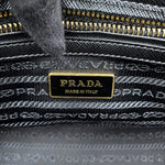 Close-up of a Prada interior label reading 'PRADA MADE IN ITALY' in gold on a black plaque, with a black and gray woven textile and gold zipper visible around it.