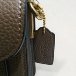 Close-up of COACH leather hangtag and brass hardware on Dark Stone Tabby bag