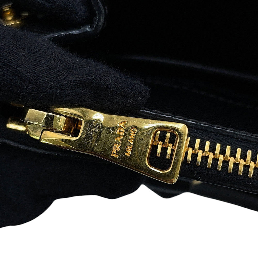 Close-up of a black leather zipper with a gold-tone metal pull engraved with 'PRADA MILANO”, detailing minor scratches on zipper surface 